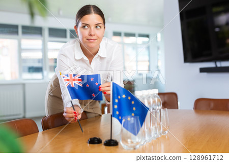 Young woman puts New Zealand and EU flags on table in office Young woman puts New Zealand and EU flags on table in office 128961712