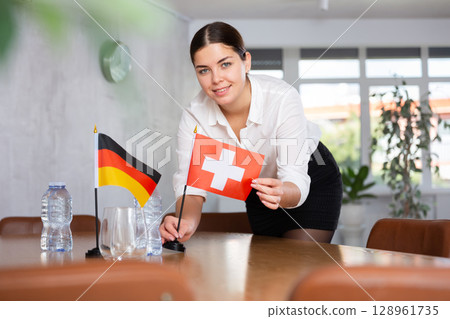 Young female attendant putting up flags for international negotiations between germany and switzerland 128961735