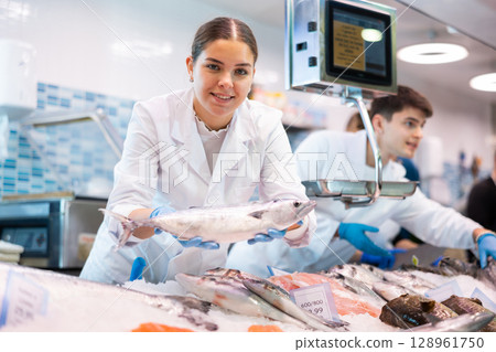 Positive saleswoman demonstrating bonito fish in fish store 128961750