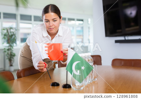 Positive young woman putting little flag of Bahrain on table next to the flag of Pakistan 128961808