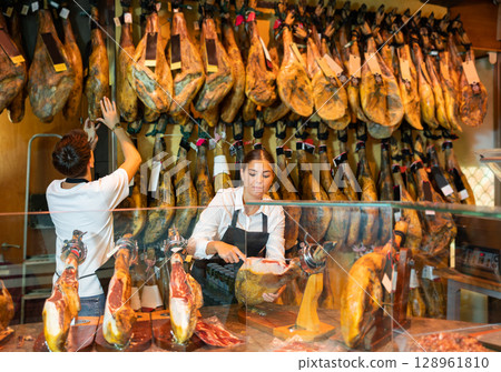 Butcher shop owner and assistant sell Spanish ham Butcher shop owner and assistant sell Spanish ham 128961810