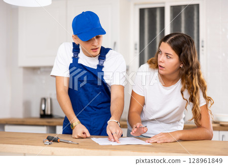 Positive plumber tells an young housewife where to sign an invoice for work performed. 128961849
