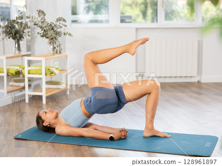 Young woman doing One Legged Bridge Pose in yoga studio Young woman doing One Legged Bridge Pose in yoga studio 128961897