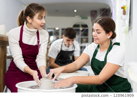 Two young women sculpt product on potter's wheel Two young women sculpt product on potter's wheel 128961909