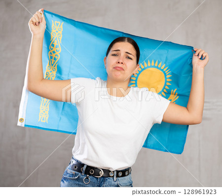 Sad young woman holding Kazakhstan flag against unicoloured background 128961923
