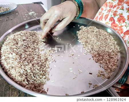 woman Hand Sorting of Rice Grains on a Steel Plate in traditional way 128961924