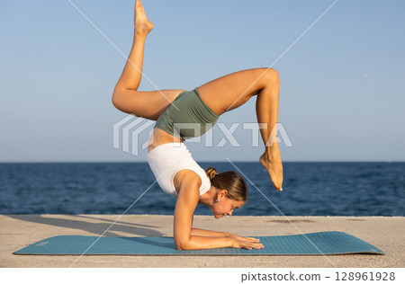Sportive girl practicing forearm stand pose of yoga on seashore 128961928