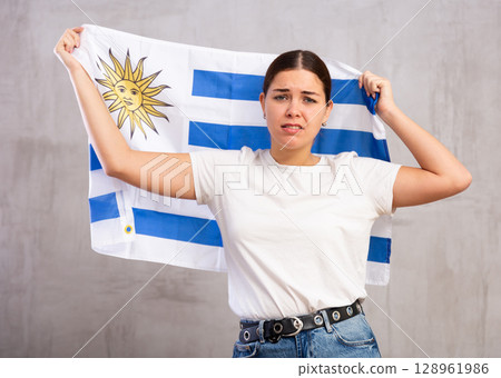 Irritated girl stands with flag of Uruguay. Isolated on gray background 128961986