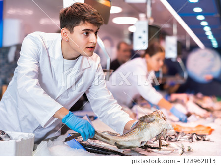 Positive salesman demonstrating cod in fish store Positive salesman demonstrating cod in fish store 128962013