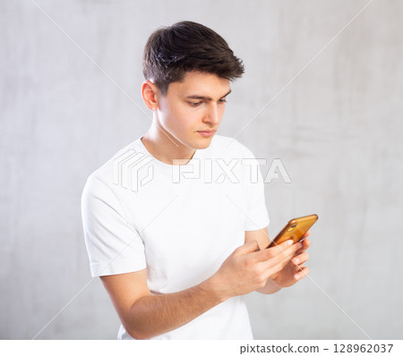 Emotional male student writing message on smartphone screen 128962037