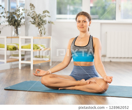 Lover of active lifestyle on yoga mat perform doing variations of padmasan in gym Lover of active lifestyle on yoga mat perform doing variations of padmasan in gym 128962052
