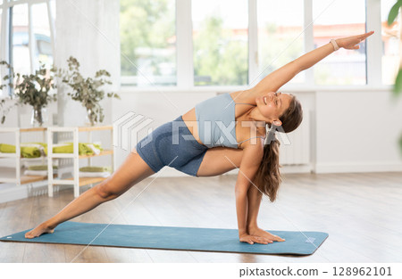 Lover of active lifestyle on yoga mat perform doing elongated side angle in gym 128962101