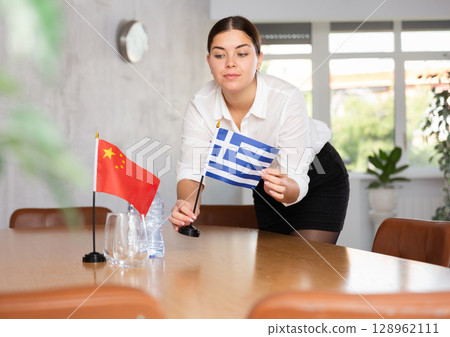Preparing for business negotiations - woman sets small flags of countries of China and Greece on table Preparing for business negotiations - woman sets small flags of countries of China and Greece on table 128962111