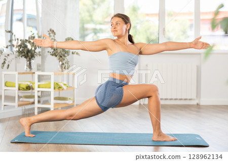 Sportive girl practicing warrior pose of yoga in light room 128962134