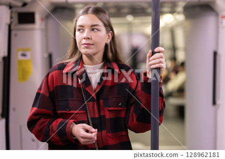 woman stands in a subway car and holds on to a handrail 128962181
