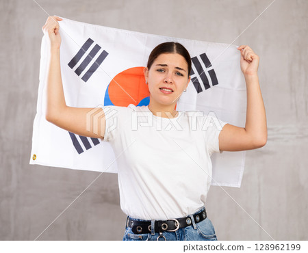 Irritated girl stands with flag of South Korea. Isolated on gray background 128962199