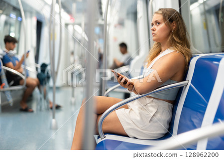 Young woman is sitting in subway car with phone, getting to work, school. 128962200