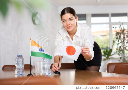 Young female attendant putting up flags for international negotiations between india and japan Young female attendant putting up flags for international negotiations between india and japan 128962347