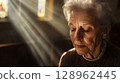 Elderly woman with eyes closed, receiving communion in church, soft beams of light surrounding her . 128962445