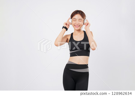 Dance is in her spirit as this fit young woman enjoys music in sportswear. Moments later, she begins to dance again, lost in rhythm and full of fitness motivation. isolated studio white background Dance is in her spirit as this fit young woman enjoys music in sportswear. Moments later, she begins to dance again, lost in rhythm and full of fitness motivation. isolated studio white background 128962634