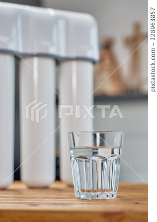 Modern water filtration system with three cartridges and glass of clean water on kitchen table. Home water purification, healthy lifestyle and drinking water safety concept 128963857