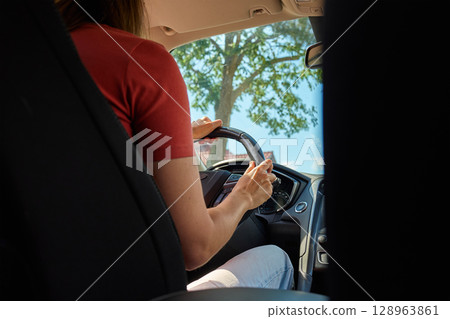 Rear view of woman holding steering wheel while driving on sunny road. Female driver in vehicle. Concept of freedom, travel and road trip 128963861