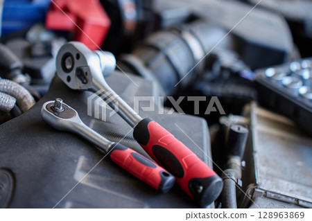 Close-up of wrench socket tool lying on car engine during maintenance work. Vehicle repair concept Close-up of wrench socket tool lying on car engine during maintenance work. Vehicle repair concept 128963869