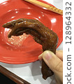 Closeup of a hand holding a braised duck foot, a Chinese delicacy. 128964332