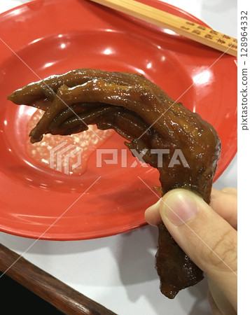 Closeup of a hand holding a braised duck foot, a Chinese delicacy. Closeup of a hand holding a braised duck foot, a Chinese delicacy. 128964332