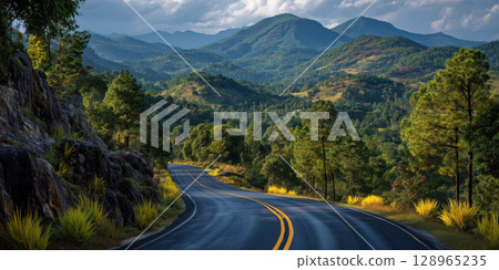 Winding asphalt road through lush green mountains and forests under cloudy sky, creating serene and picturesque landscape 128965235