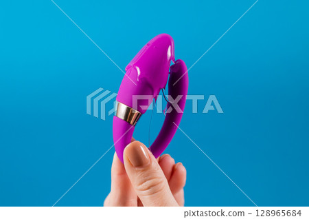 A woman holds a curved sex toy in lubrication on a blue background. Vaginally clitoral vibrator.  128965684