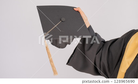 Hand of an elderly woman with a graduation hat on a white background. Hand of an elderly woman with a graduation hat on a white background. 128965690