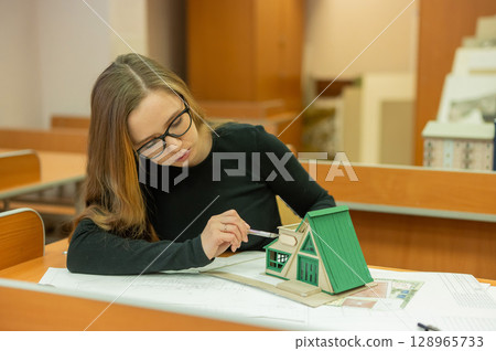 Caucasian young woman making a model of a building. Student of the construction university.  128965733