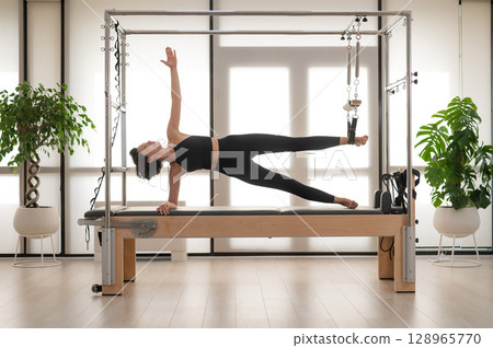 Asian woman doing pilates on reformer.  128965770