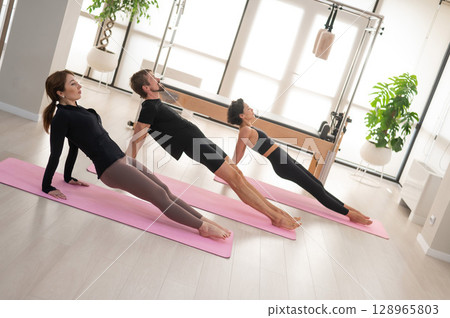 Two women and a man are doing yoga in the studio. 128965803