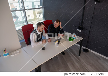 Two Caucasian men sitting at a table and discussing work.  128965985