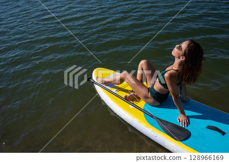Beautiful caucasian woman is swimming on a SUP board. 128966169