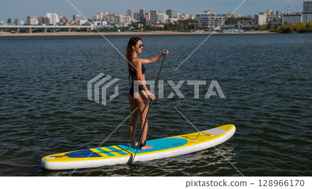 Caucasian woman riding a SUP board on the lake. Summer sport. 128966170