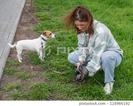 A woman cleans up dog excrement while on a walk. 128966192