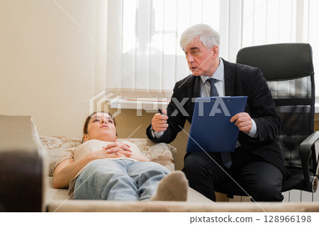 Caucasian woman lies on a couch at a reception with a psychotherapist. An elderly man works as a psychiatrist 128966198