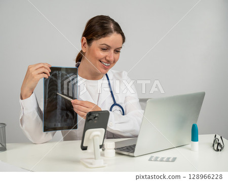Telemedicine. Caucasian female doctor communicates with patient on laptop and shows x-ray of lungs. Telemedicine. Caucasian female doctor communicates with patient on laptop and shows x-ray of lungs. 128966228