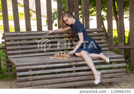 Caucasian woman playing chess outdoors. 128966292