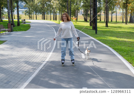 Caucasian woman roller skating with her jack russell terrier dog in park. Caucasian woman roller skating with her jack russell terrier dog in park. 128966311