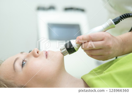 Caucasian woman undergoing radio wave RF lifting procedure in beauty salon. Caucasian woman undergoing radio wave RF lifting procedure in beauty salon. 128966360