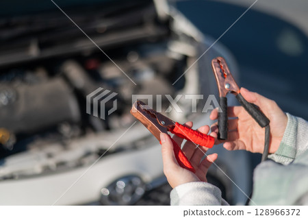 Woman holding clamps for charging a car battery. Woman holding clamps for charging a car battery. 128966372