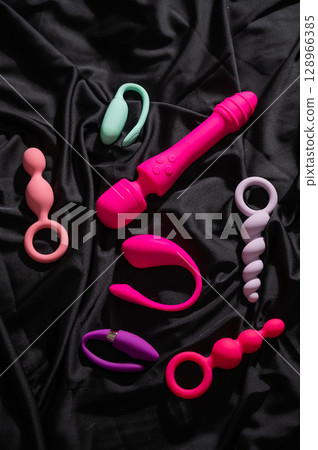 Collection of sex toys on a black sheet. Top view of various vibrators.  128966385