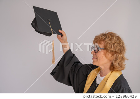 An elderly woman holds a graduation hat.  128966429