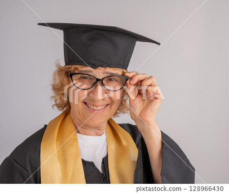 Portrait of an elderly woman in a graduation gown on a white background. Portrait of an elderly woman in a graduation gown on a white background. 128966430