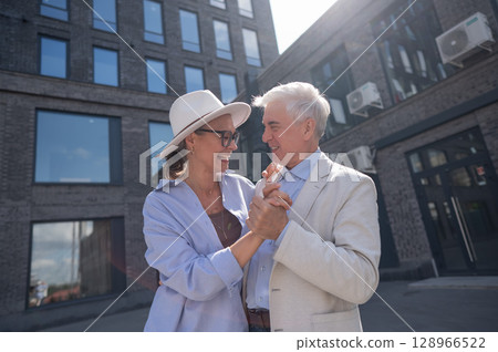 An elderly couple in love dances outdoors. A gray-haired man and a mature woman laugh and hug. An elderly couple in love dances outdoors. A gray-haired man and a mature woman laugh and hug. 128966522