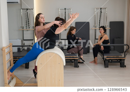 Three women doing Pilates on a reformer and a Pilates barrel.  128966543
